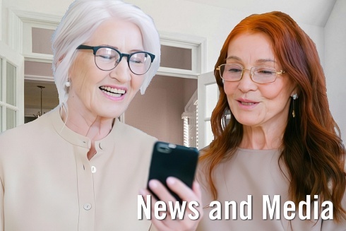 two older women stand next to eachother while looking at a cell phone with the words news and media embedded on screen. 