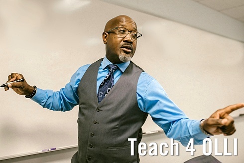 a man stands at a white board point out to class