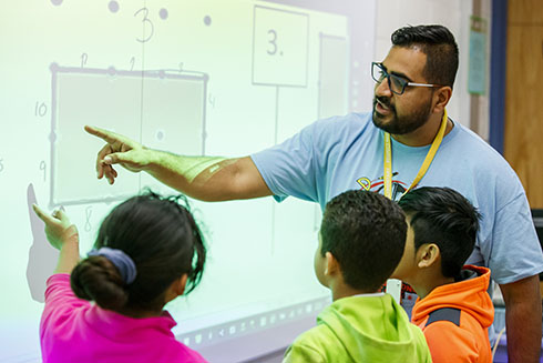 Teacher instructing students at a digital whiteboard in a classroom