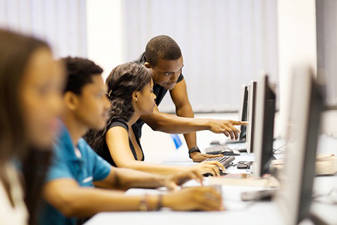 Black male teacher with students at computers in a classroom