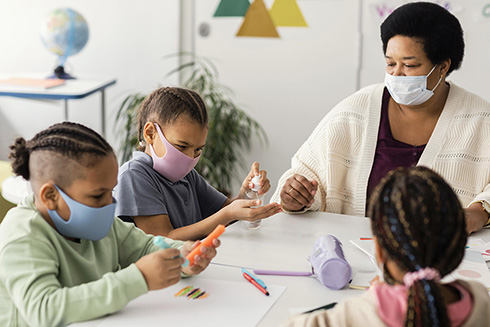 Kids with a teacher in a classroom disinfecting a table