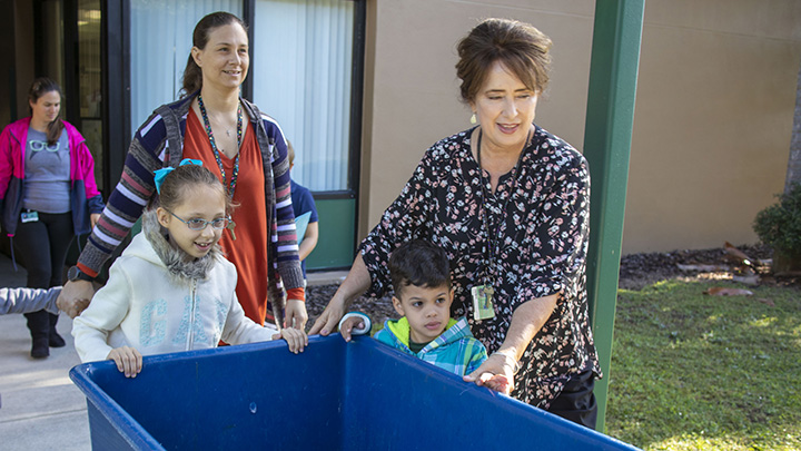 Teachers help students in an ESE classroom push a large bin around their school to collect recyclables