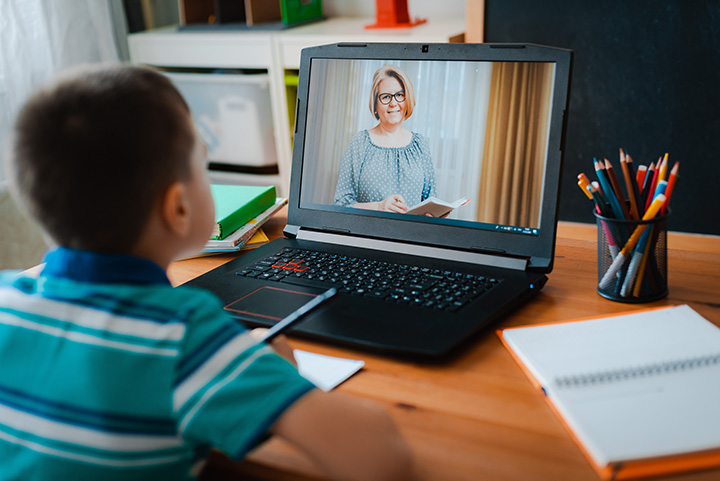 young boy studies at home on laptop with teacher