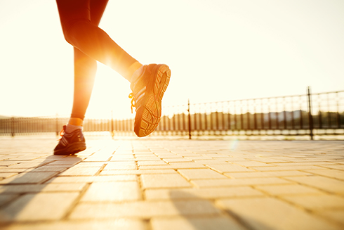 A person's feet while they run outside at sunset