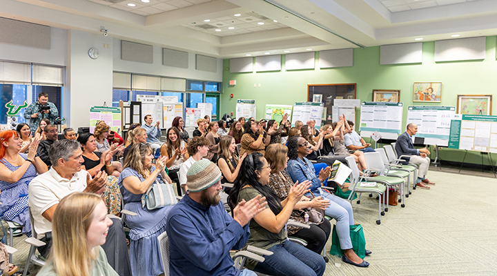 TECO Halll with posters along the walls for presentation, people seated facing speaker in front of the room