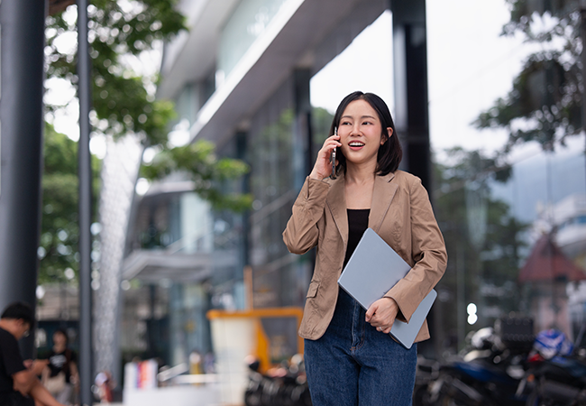 a woman outside of office building holding laptop talks on mobile phone