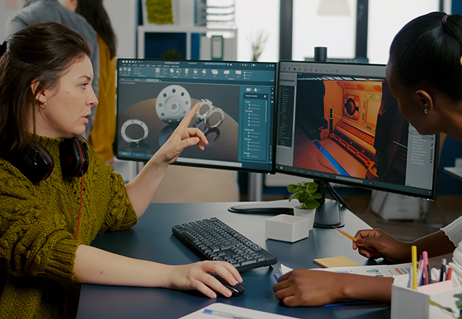 woman showing another woman a game on a computer monitor