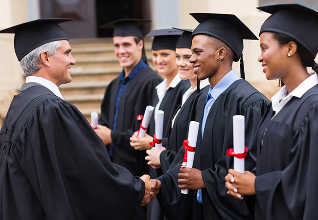 faculty member shaking hands with graduate while other graduates look on
