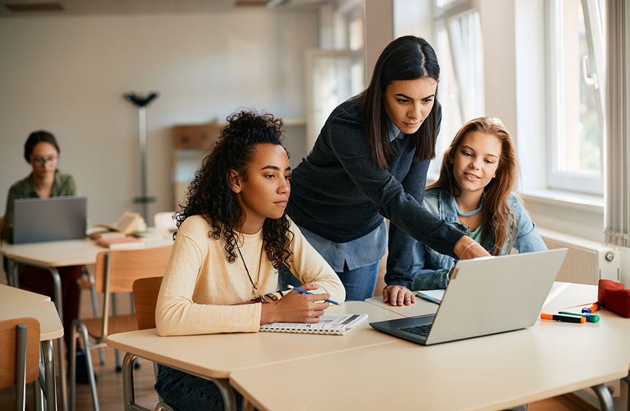teacher helping two female students in a classroom