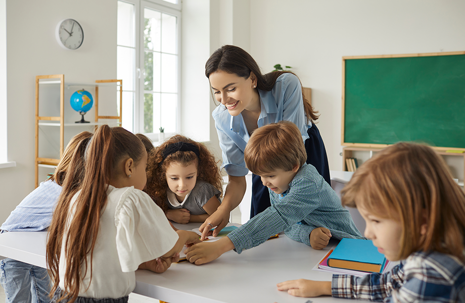 smiling teacher helping young students in classroom