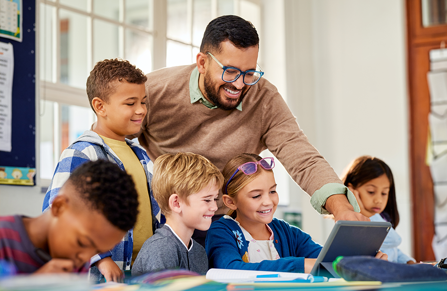 smiling teacher helping young students in classroom