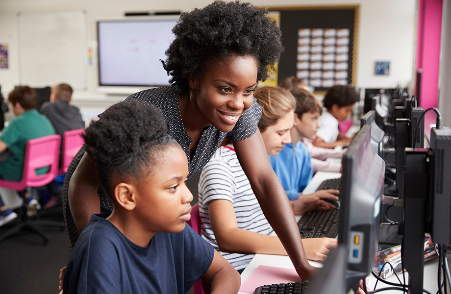 teacher helping young student on computer in classroom