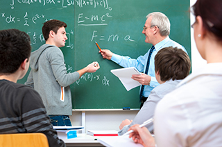 teacher with students in classroom completing physics equations on a chalkboard