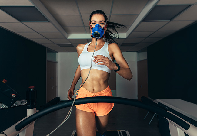 a woman runs on a treadmill with a max on her face gathering data. A Vomax machine