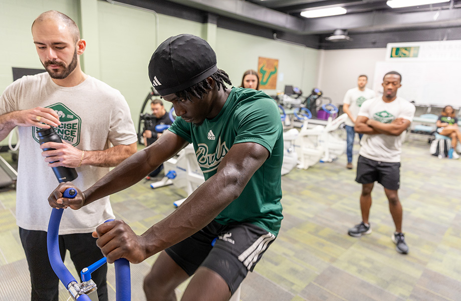 a usf student athlete rides on a exercise bike with docotors around 