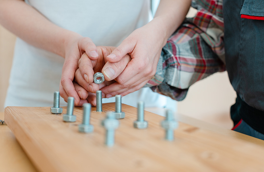close up of a pair of hands helping an older set of hands put nuts on screws