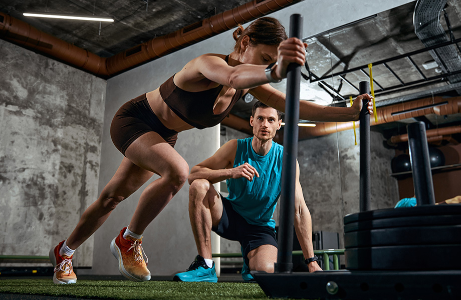 a women pushes a weighted sled with a man coaching in the background