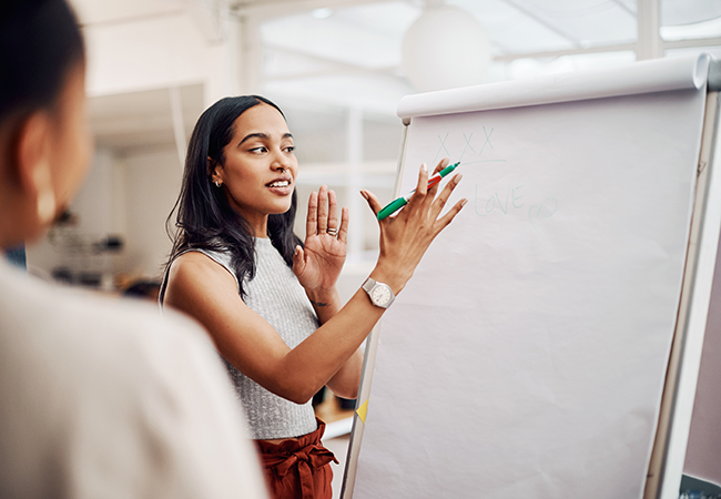 a woman stands at a large paper describing someting with pen in hand