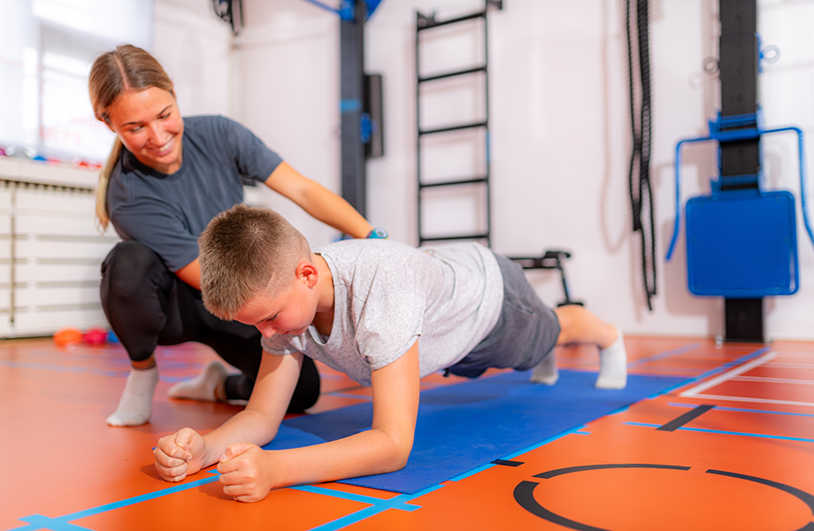 a woman instructor shows a young boy how to hold his form while planking