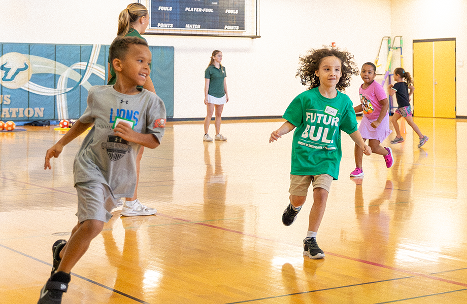 a group of young kids run around a gym with smiles on their faces