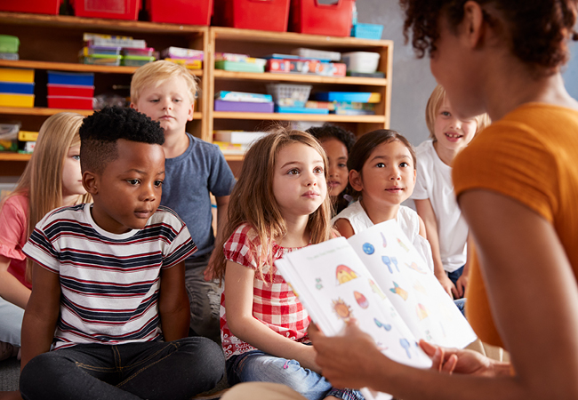 A woman teacher sits and reads to her young students