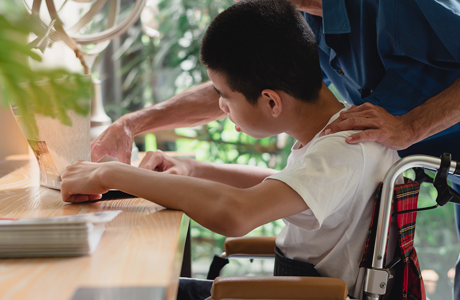 a young boy with special needs in a wheel chair sits at a desk