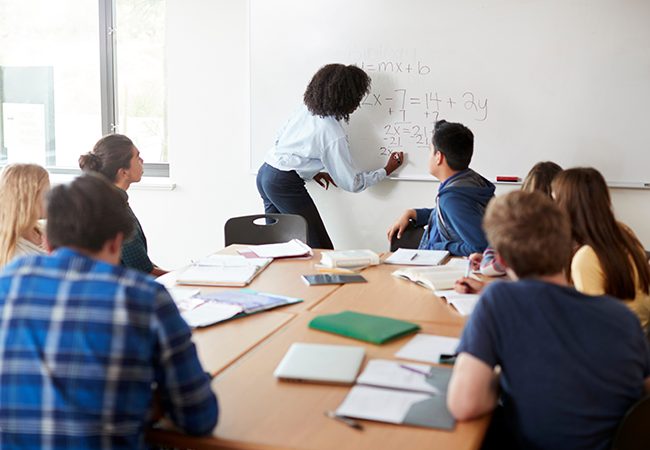 a teacher does a math equation on the front of a classroom of students
