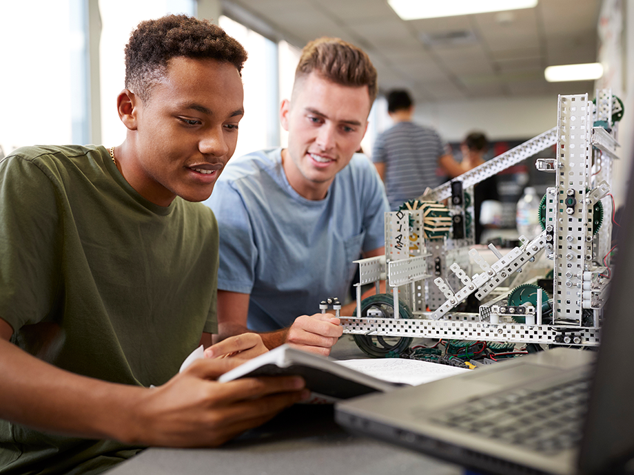 two older students sit at computer while building something with metal in science