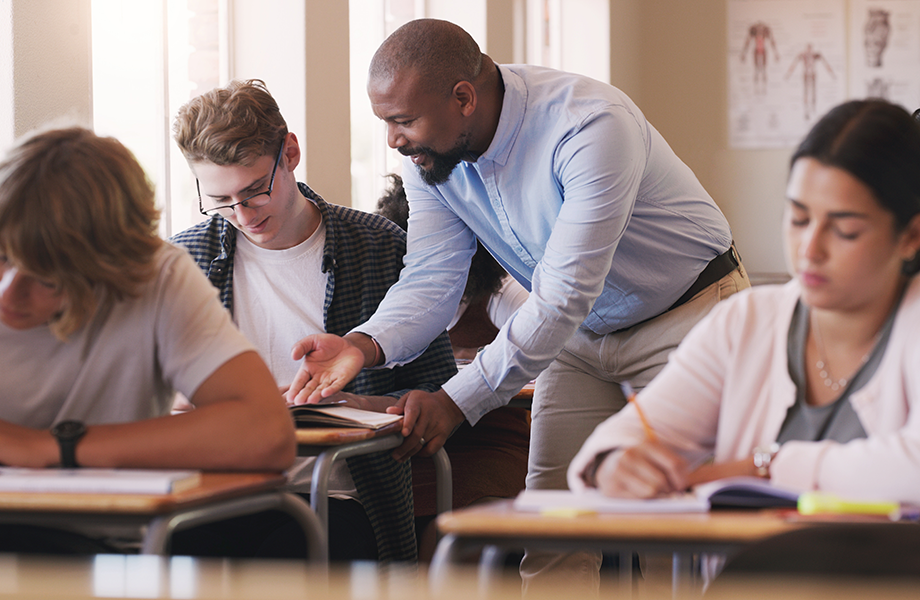 A teach leans over to help a student in class
