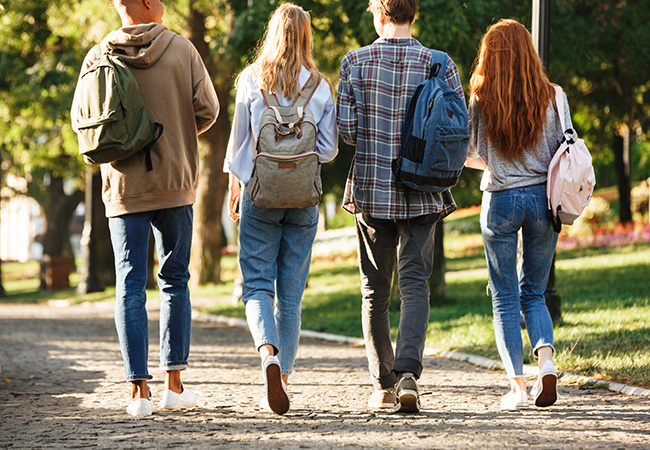 a group of college students in backpacks walk away from camera down sidewalk