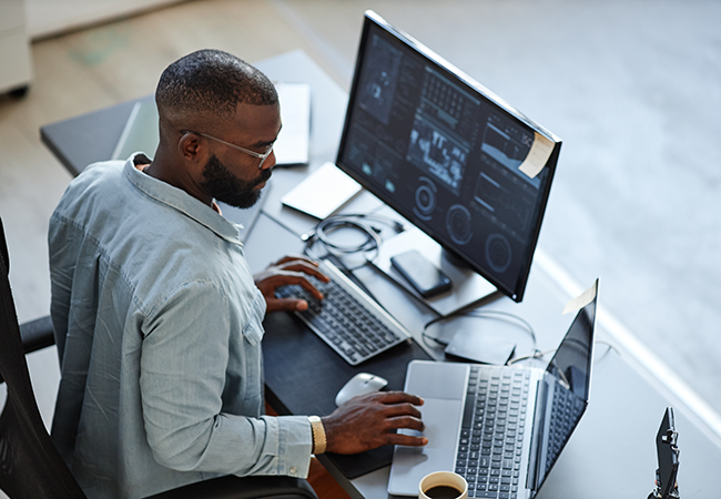 An overhead shot of a man at a desk on his computer with data on the screen