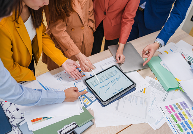 a table with lots of data tables and a close up of people hands point at charts and graphs