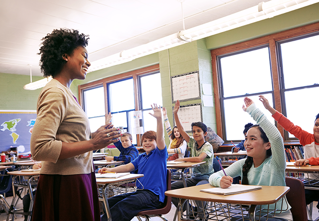 a teacher stands at front of class taking questions from students