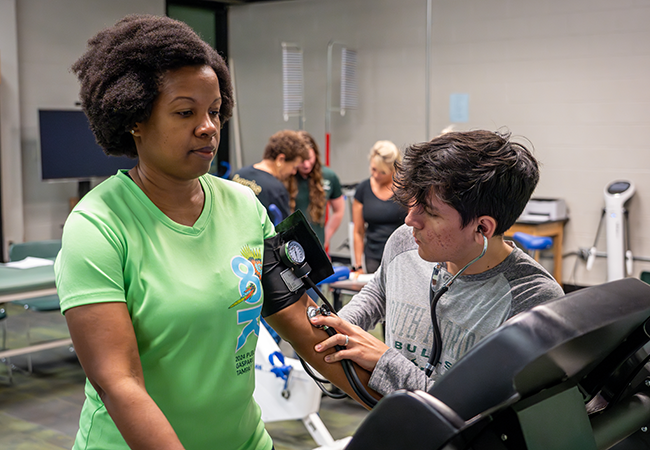 a usf exercise science student helps a patient on the tredmil and takes he blood pressure as she walks