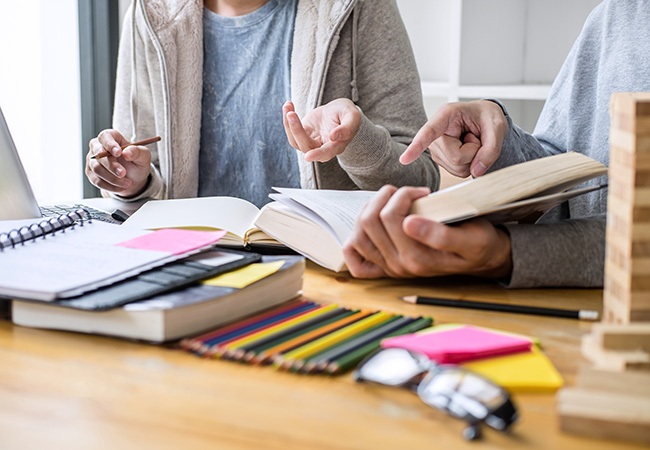 a close up of 2 people hands at a desk holding papers and pointing to items on desk