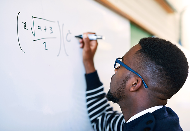 a student writes a math equation on a white board