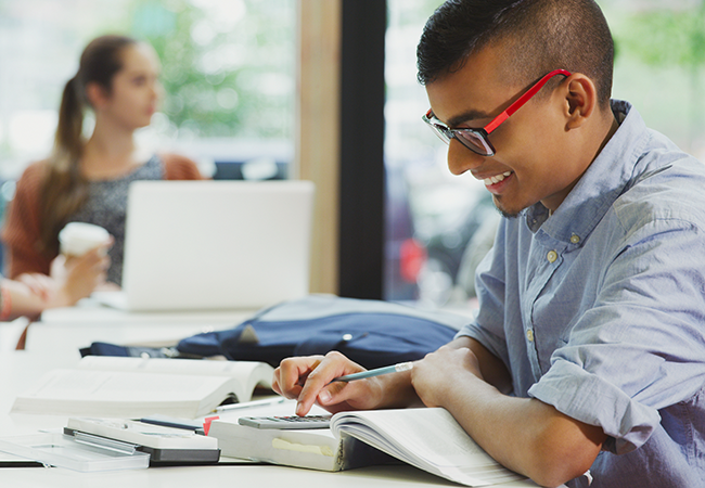 a male student smiles down at his calculater while working