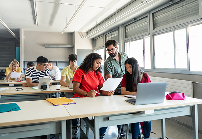a wide shot of a classroom with 3 students working together at a desk