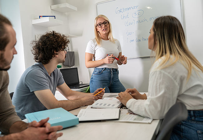 a woman stands in front of others sitting at table talking