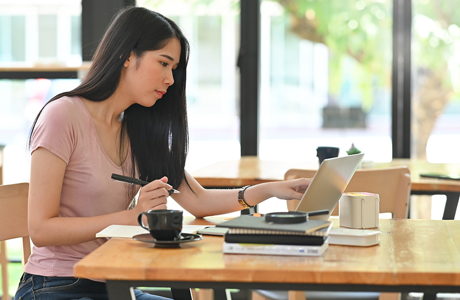 Young female working on laptop and holding pen on table