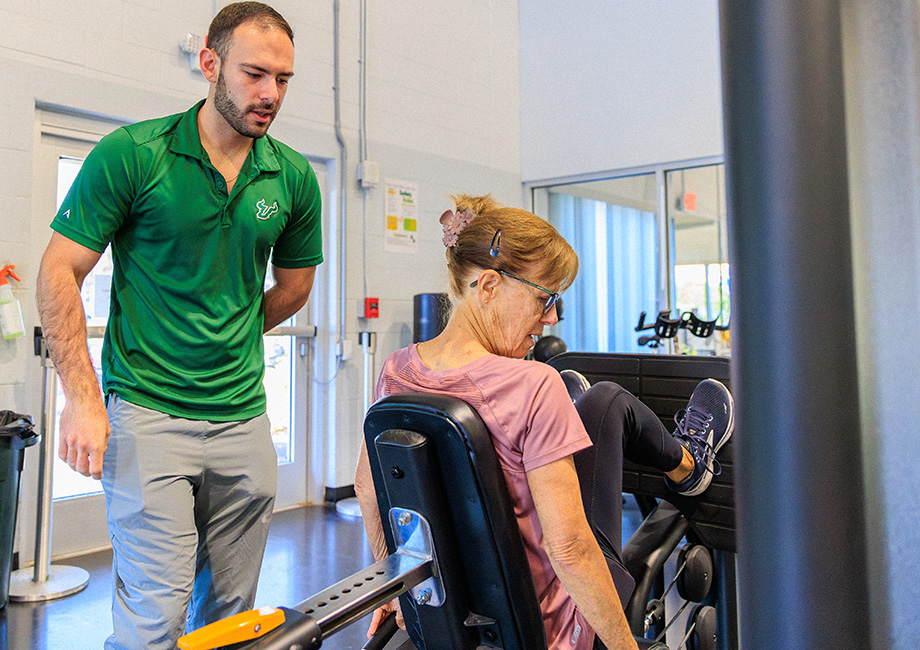a man stands over a woman instructing her on a gym machine