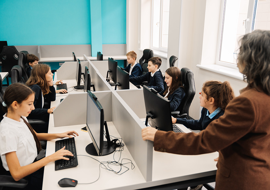 a woman teacher stands in front of a computer class of middle school students