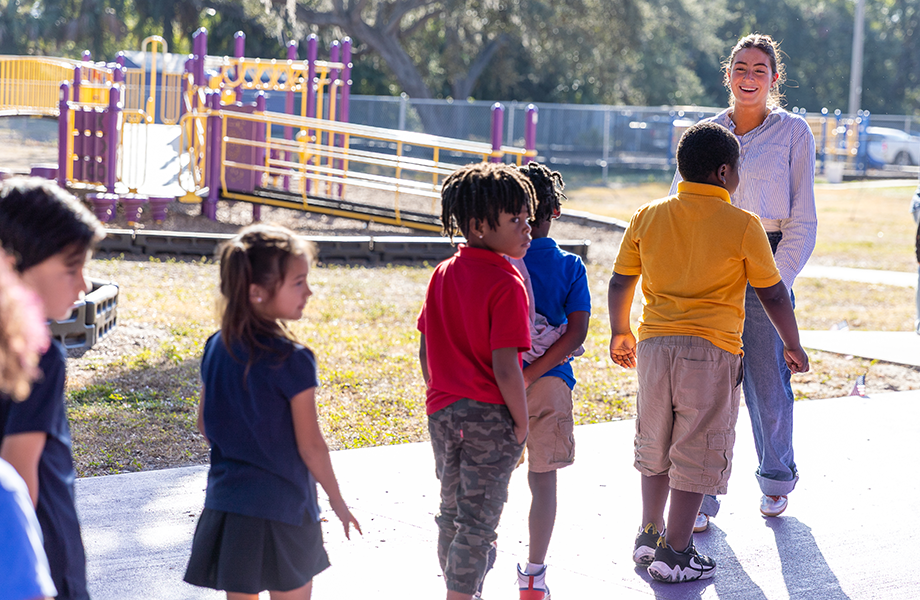 a woman teacher leads a class in line after recess smiling