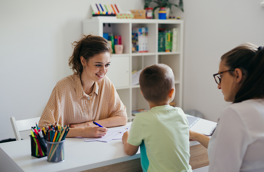 a working professional sits behind a desk taking notes with a mom and a young child on the other side of the desk