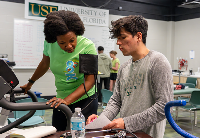 a usf student works with patient on a treadmill showing her a clipboard with data