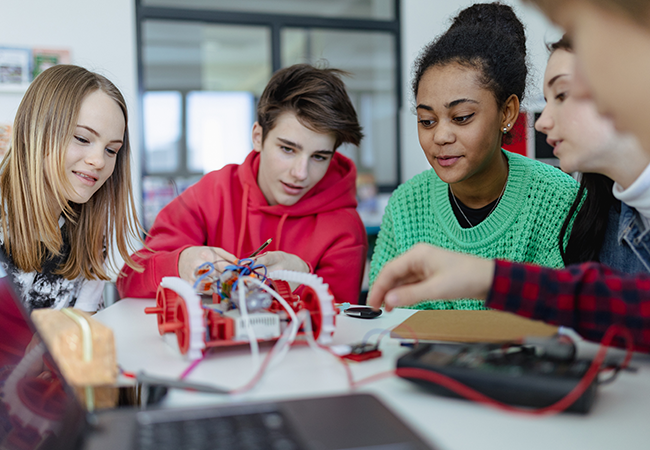 a group of students sitting a table working with robots