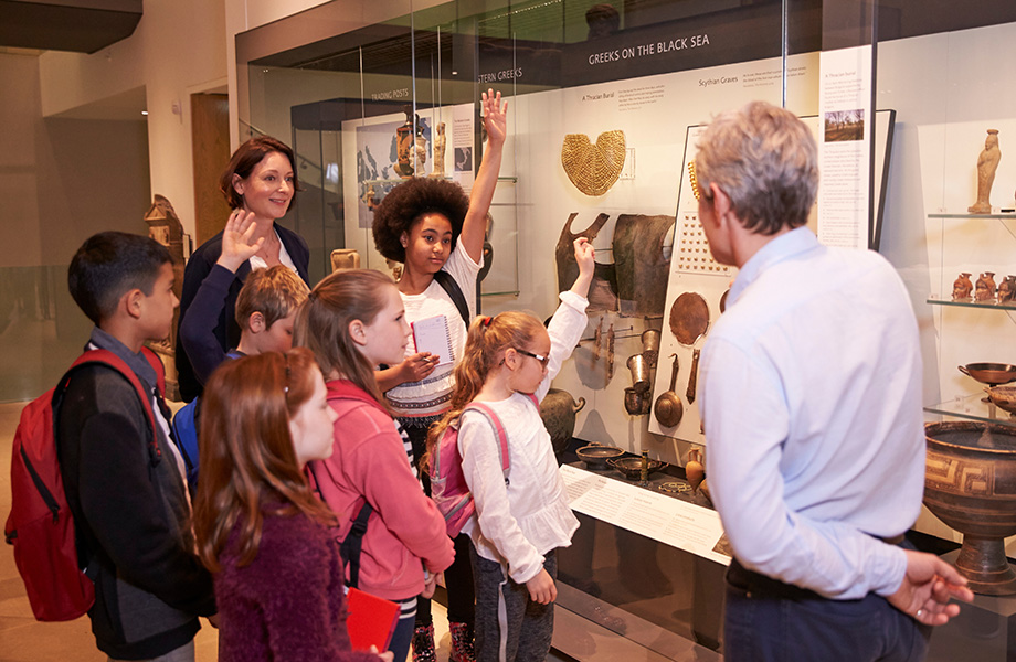 a museum coordniator stands in front of a tour group of kids showing them a museum