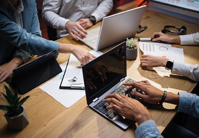 a close up of a group of people sitting at a desk with laptops and data sheets