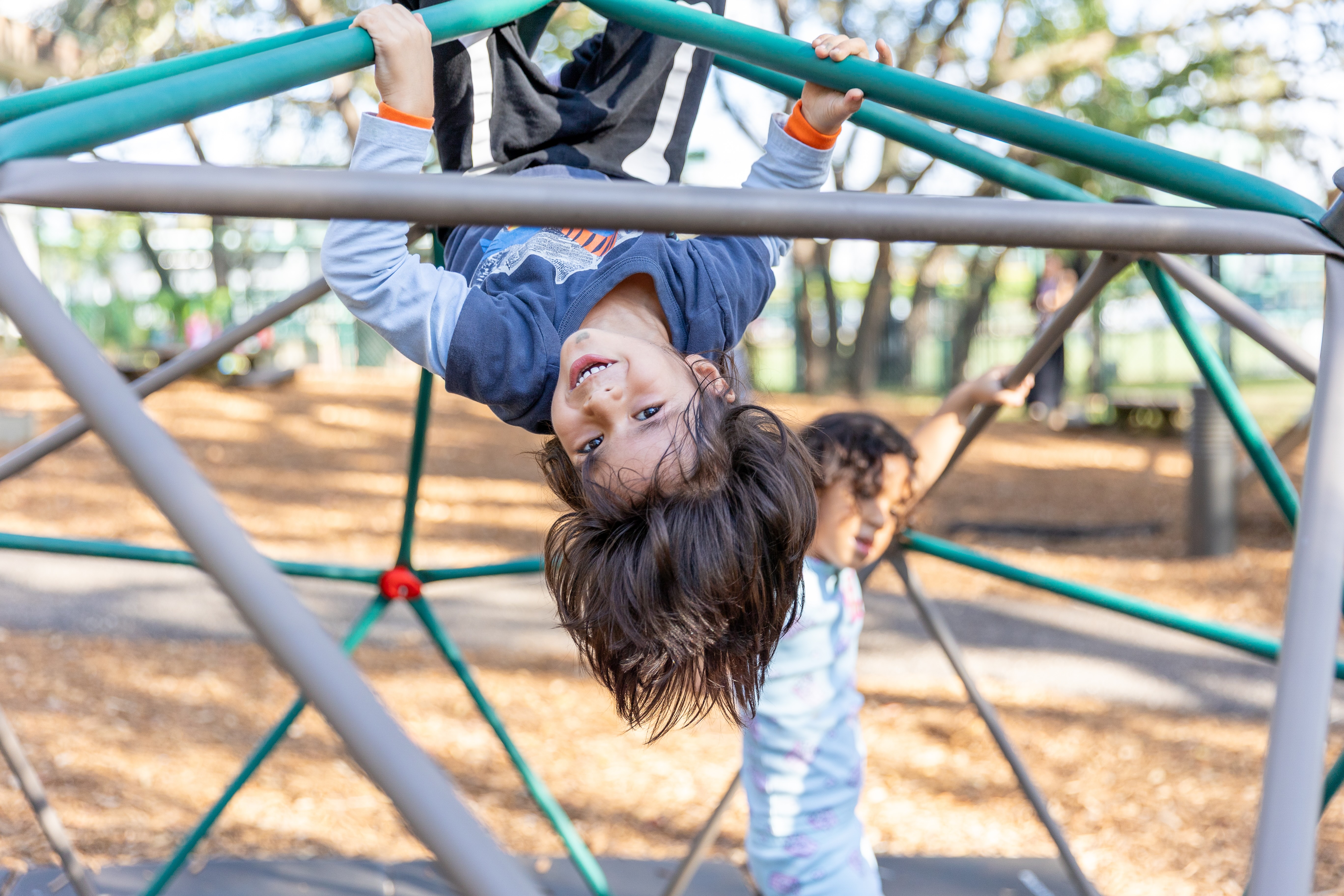 little boy hanging upside down on jungle gym