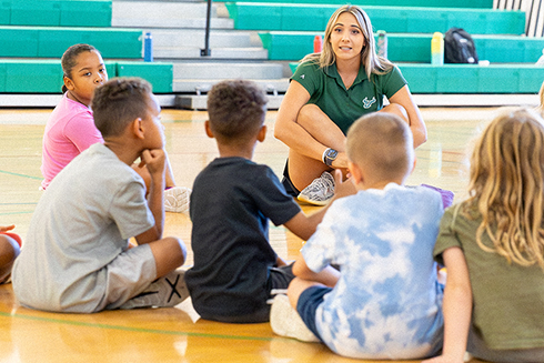 USF physical education student sitting down with homeschooled students in USF gymnasium